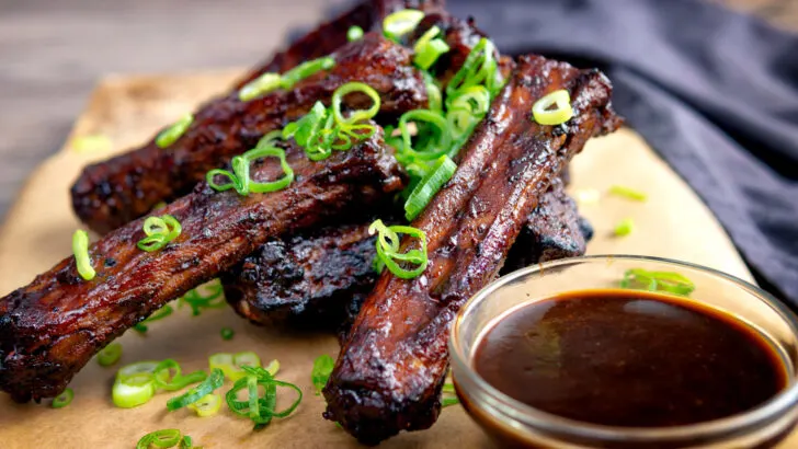 Chinese takeaway style spare ribs with a dipping sauce and sliced spring onions.