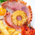Overhead close-up gammon steak, pineapple, egg, chips with tomato and peas.