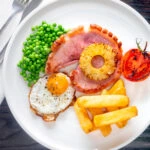 Overhead gammon steak, pineapple, egg, chips with tomato and peas.
