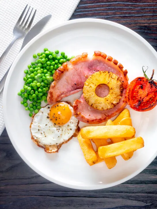 Overhead gammon steak, pineapple, egg, chips with tomato and peas.