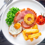 Overhead gammon steak, pineapple, egg, chips with tomato and peas featuring a title overlay.