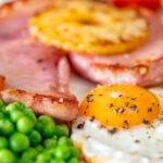 Close-up gammon steak, pineapple, egg, chips with tomato and peas.