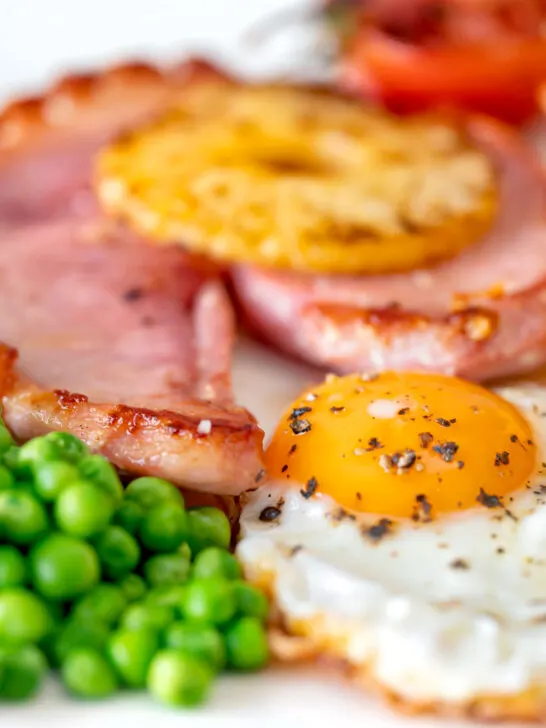 Close-up gammon steak, pineapple, egg, chips with tomato and peas.