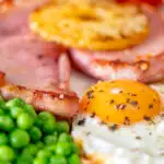 Close-up gammon steak, pineapple, egg, chips with tomato and peas featuring a title overlay.