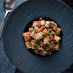 Overhead haggis pasta bolognese with mezzi rigatoni in red wine sauce with cherry tomatoes featuring a title overlay.