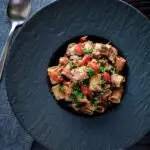 Overhead haggis pasta bolognese with mezzi rigatoni in red wine sauce with cherry tomatoes featuring a title overlay.