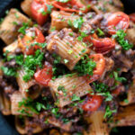 Overhead close up haggis pasta bolognese with mezzi rigatoni with cherry tomatoes.