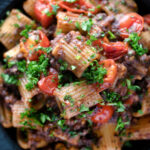 Overhead close up haggis pasta bolognese with mezzi rigatoni with cherry tomatoes featuring a title overlay.