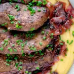 Close up overhead fried lambs liver and port onions on polenta featuring a title overlay.