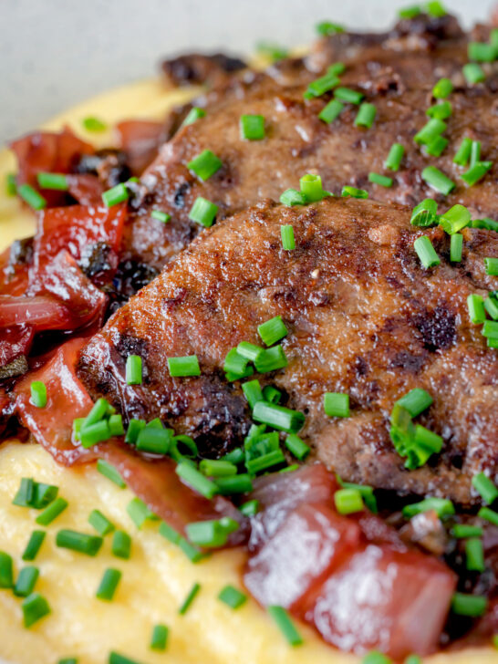 Close up fried lambs liver and port onions on polenta with chives.