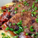 Close up fried lambs liver and port onions on polenta with chives featuring a title overlay.