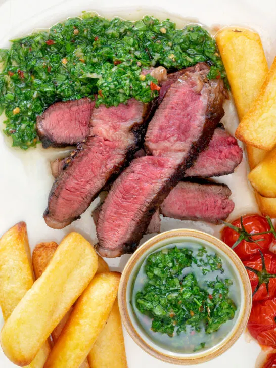 Overhead close-up rare cooked rump steak with chimichurri sauce and chips.