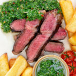 Overhead close-up rare cooked rump steak with chimichurri sauce and chips featuring a title overlay.