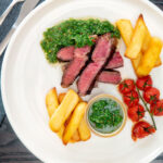 Overhead rare cooked rump steak with chimichurri sauce, tomatoes and chips.