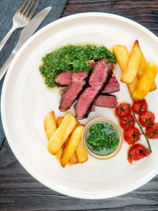 Overhead rare cooked rump steak with chimichurri sauce, tomatoes and chips.