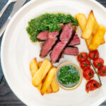 Overhead rare cooked rump steak with chimichurri sauce, tomatoes and chips.