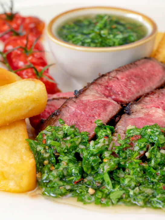 Close-up rare cooked rump steak with chimichurri sauce, tomatoes and chips.