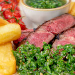 Close-up rare cooked rump steak with chimichurri sauce, tomatoes and chips featuring a title overlay.