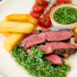 Rare cooked rump steak with chimichurri sauce, tomatoes and chips.