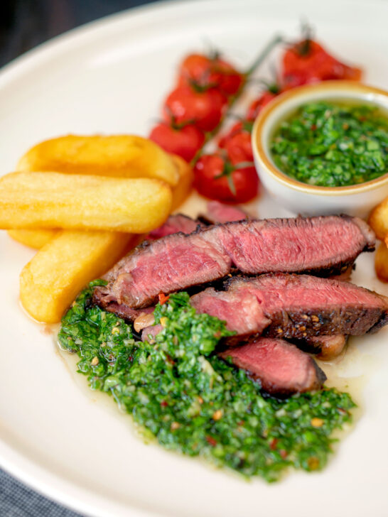 Rare cooked rump steak with chimichurri sauce, tomatoes and chips.