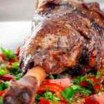 Close up slow cooker braised lamb shanks in a red wine, tomato, garlic and pepper sauce.