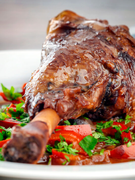 Close up slow cooker braised lamb shanks in a red wine, tomato, garlic and pepper sauce.