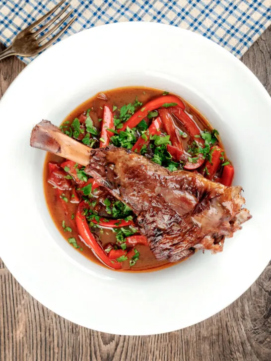 Overhead slow cooker braised lamb shanks in a red wine, tomato, garlic and pepper sauce.