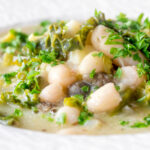 Close-up vegan cabbage and cannellini bean soup with potatoes and capers.