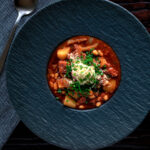 Overhead corned beef stew with baked beans and potatoes featuring a title overlay.