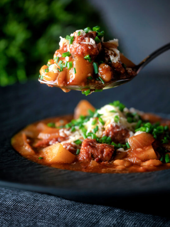 Spoon of corned beef stew with baked beans and potatoes.