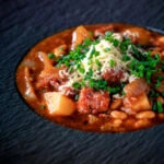 Close-up corned beef stew with baked beans and potatoes.