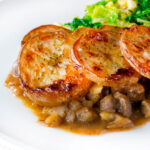 Close-up scalloped potato topped Lancashire hotpot with buttered cabbage on a plate.