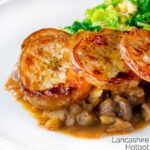 Close scalloped potato topped Lancashire hotpot with buttered cabbage on a plate featuring a title overlay.