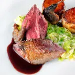 Close-up roast pigeon crown, confit legs, red wine sauce, cabbage and fondant potatoes.