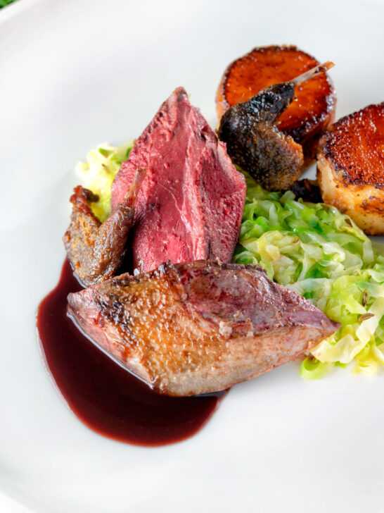 Close-up roast pigeon crown, confit legs, red wine sauce, cabbage and fondant potatoes.
