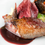 Close-up roast pigeon breasts, confit legs and red wine sauce.