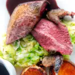 Overhead close-up roast pigeon breasts, confit legs, red wine sauce, buttered cabbage and fondant potatoes.