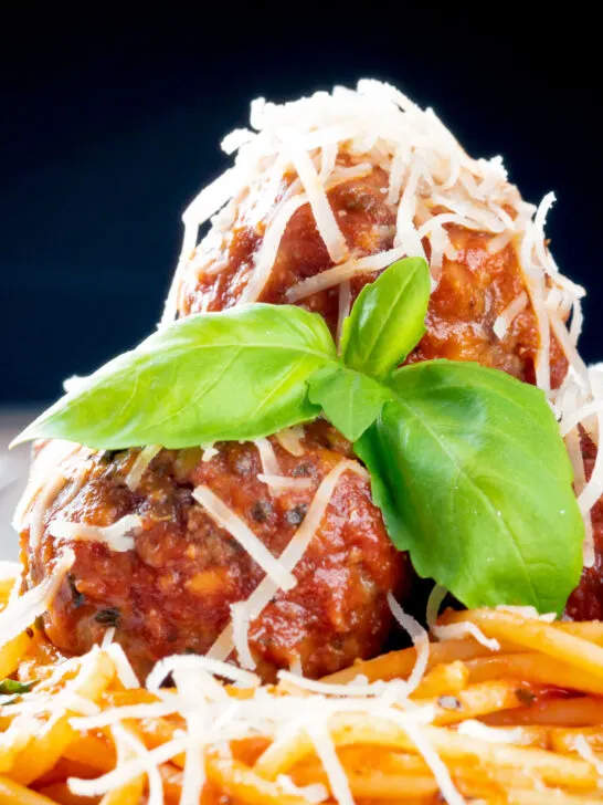 Close-up pasta with meatballs, grated parmesan cheese and basil.