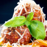 Close up pasta with meatballs, grated parmesan cheese and basil featuring a title overlay.