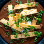 Overhead spicy vegan black bean soup topped with crispy tortillas and fresh coriander.