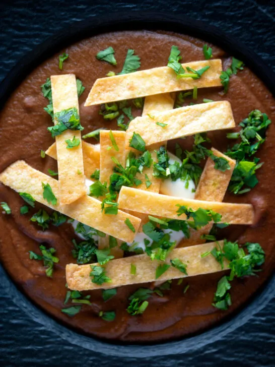 Overhead spicy vegan black bean soup topped with crispy tortillas and fresh coriander.