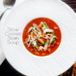 Overhead slow cooker bean and tomato soup with balsamic vinegar featuring a title overlay.