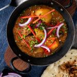 Overhead Pakistani aloo gosht meat and potato curry served with a naan bread.