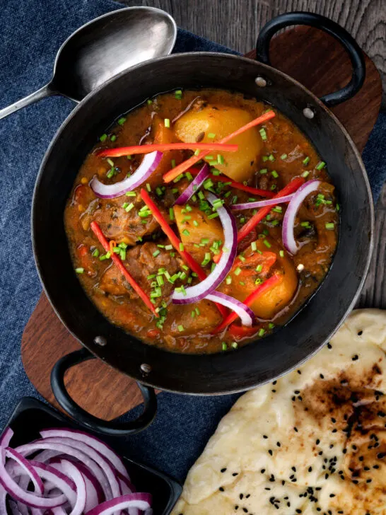 Overhead Pakistani aloo gosht meat and potato curry served with a naan bread.