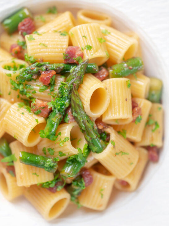 Close-up overhead bacon and asparagus pasta with mezzi rigatoni and fresh parsley.