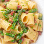 Close-up overhead bacon and asparagus pasta with mezzi rigatoni and fresh parsley featuring a title overlay.