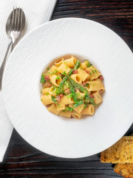 Overhead bacon and asparagus mezzi rigatoni and fresh parsley.