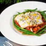 White fish baked in tomato sauce with green beans amandine featuring a title overlay.