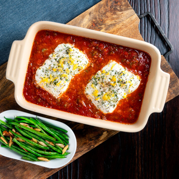 Baked cod in tomato sauce with thyme, rosemary and lemon in a baking dish.