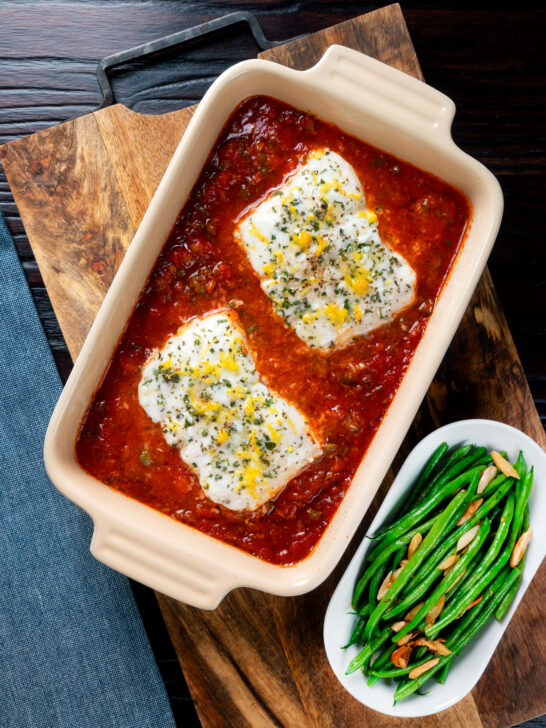 Overhead baked cod with tomato sauce served with green bean amandine.